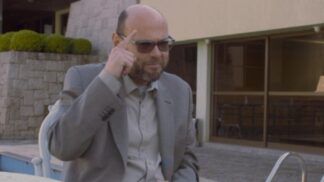 Foto de Marcelo (homem careca de terno), apontando para a cabeça durante entrevista