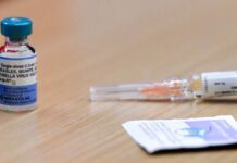 Foto de uma seringa e uma dose de vacina contra sarampo em cima de uma mesa de madeira