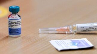 Foto de uma seringa e uma dose de vacina contra sarampo em cima de uma mesa de madeira