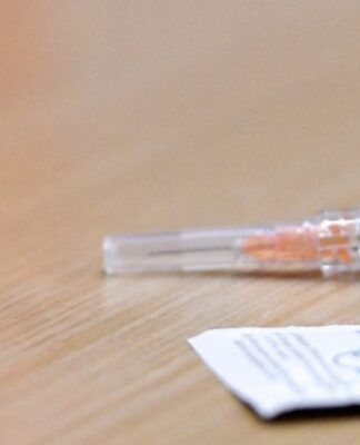 Foto de uma seringa e uma dose de vacina contra sarampo em cima de uma mesa de madeira