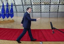 Macron caminha sobre tapete vermelho com bandeiras da União Europeia ao fundo