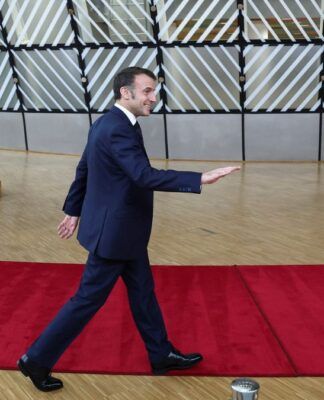 Macron caminha sobre tapete vermelho com bandeiras da União Europeia ao fundo