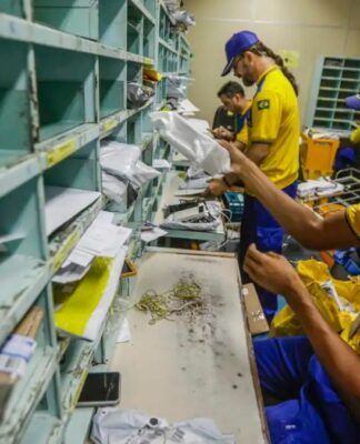 Funcionários dos Correios, uniformizados, manuseiam correspondências dentro de uma sala