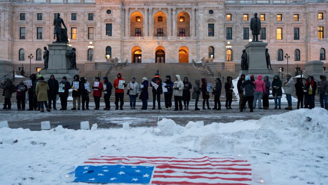 Manifestantes participam de vigília à luz de velas em frente ao Capitólio Estadual em St. Paul, Minnesota, com a bandeira dos EUA colocada sobre a neve