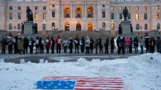 Manifestantes participam de vigília à luz de velas em frente ao Capitólio Estadual em St. Paul, Minnesota, com a bandeira dos EUA colocada sobre a neve