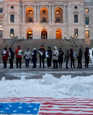 Manifestantes participam de vigília à luz de velas em frente ao Capitólio Estadual em St. Paul, Minnesota, com a bandeira dos EUA colocada sobre a neve
