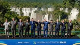 Fotografia oficial dos presidentes e chefes de delegação dos Estados Partes do Mercosul, todos em pé, de mãos dadas, à frente das Cataratas do Iguaçu