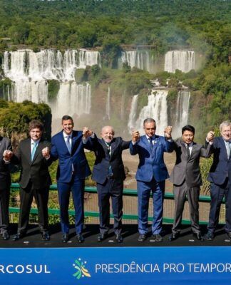 Fotografia oficial dos presidentes e chefes de delegação dos Estados Partes do Mercosul, todos em pé, de mãos dadas, à frente das Cataratas do Iguaçu