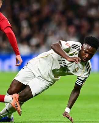 Vini Jr. está caindo no gramado após driblar jogador do Sevilla