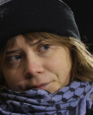 Greta Thumberg veste um gorro preto e um cachecol diante do microfone