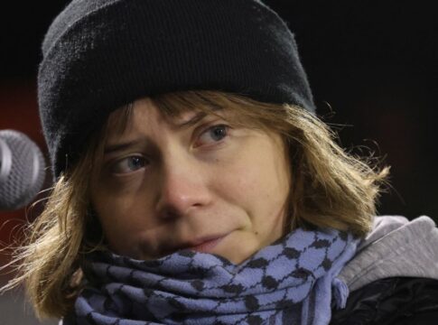 Greta Thumberg veste um gorro preto e um cachecol diante do microfone