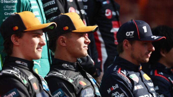 Três pilotos de automóveis sentados lado a lado, usando macacões e bonés de suas equipes de corrida. Eles olham para a frente com expressão neutra, enquanto outros membros de equipes aparecem desfocados ao fundo.