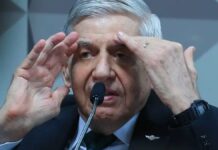 Homem de cabelos grisalhos fala ao microfone em ambiente oficial, gesticulando com as mãos próximas ao rosto enquanto usa terno escuro, camisa branca e gravata verde.