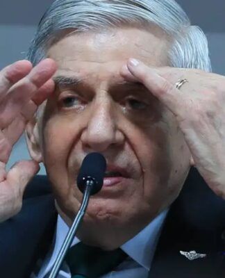 Homem de cabelos grisalhos fala ao microfone em ambiente oficial, gesticulando com as mãos próximas ao rosto enquanto usa terno escuro, camisa branca e gravata verde.