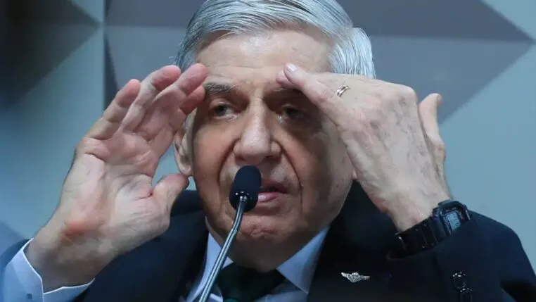 Homem de cabelos grisalhos fala ao microfone em ambiente oficial, gesticulando com as mãos próximas ao rosto enquanto usa terno escuro, camisa branca e gravata verde.