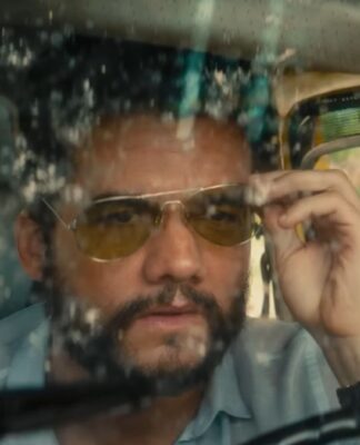 Wagner Moura em cena do filme, dentro de um carro com o vidro sujo, ajustando seu óculos escuro de lente amarelada