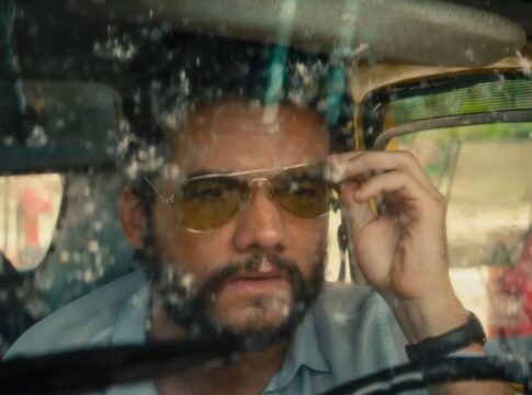 Wagner Moura em cena do filme, dentro de um carro com o vidro sujo, ajustando seu óculos escuro de lente amarelada