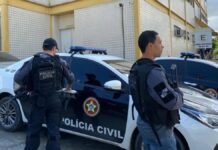 Policiais civis estão à frente de um carro da polícia