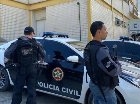 Policiais civis estão à frente de um carro da polícia