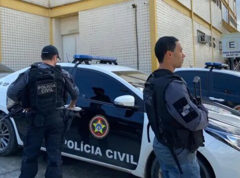 Policiais civis estão à frente de um carro da polícia