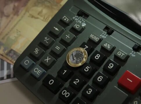 Imagem de uma moeda de um real colocada sobre uma calculadora