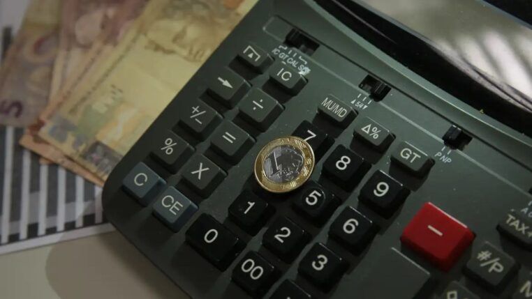 Imagem de uma moeda de um real colocada sobre uma calculadora