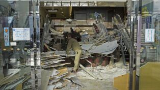 Trabalhador limpa entrada de sua loja após estrago causado por terremoto