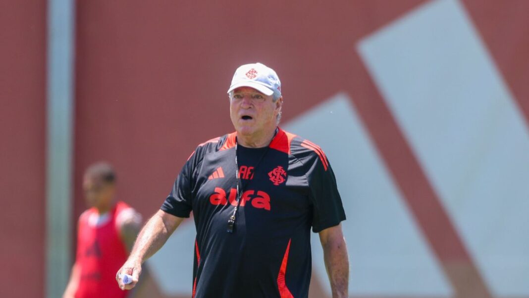 A imagem é um plano médio do técnico de futebol Abel Braga, em pé, em um campo de treinamento durante o dia, sob forte luz solar.