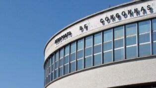 A imagem é um plano médio que foca na parte superior da fachada curva do terminal de passageiros do Aeroporto de Congonhas (CGH), em São Paulo, em um dia claro e ensolarado.