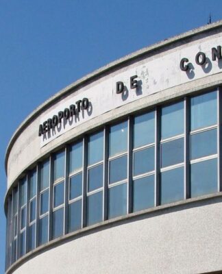 A imagem é um plano médio que foca na parte superior da fachada curva do terminal de passageiros do Aeroporto de Congonhas (CGH), em São Paulo, em um dia claro e ensolarado.