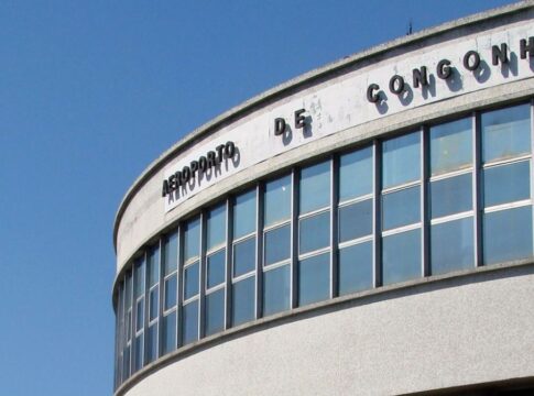 A imagem é um plano médio que foca na parte superior da fachada curva do terminal de passageiros do Aeroporto de Congonhas (CGH), em São Paulo, em um dia claro e ensolarado.