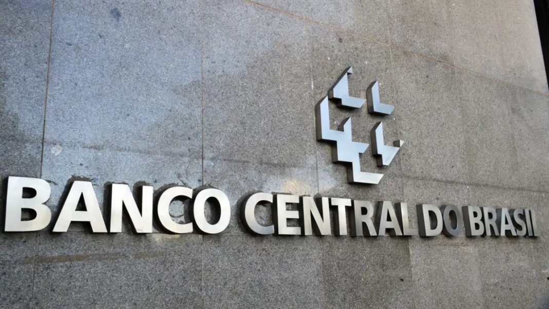 A imagem é um close-up que foca na parte central da fachada externa do edifício do Banco Central do Brasil, destacando o nome da instituição e seu símbolo em metal.