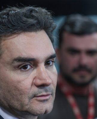 A foto é um primeiro plano (close-up) do rosto de Celso Sabino, atual Ministro do Turismo do Brasil. Ele está posicionado de três quartos, olhando para a direita da imagem com uma expressão séria e atenta, como se estivesse ouvindo uma pergunta ou concedendo uma entrevista.