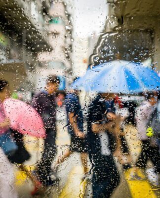 Em imagem ilustrativas, pessoas andam de guarda-chuva em tempo de chuva na rua