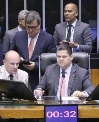 A foto mostra um grupo de parlamentares sentados e em pé, reunidos em um ambiente que se assemelha à mesa diretora ou a uma comissão dentro do Congresso Nacional .