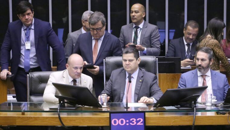 A foto mostra um grupo de parlamentares sentados e em pé, reunidos em um ambiente que se assemelha à mesa diretora ou a uma comissão dentro do Congresso Nacional .