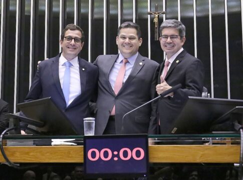 A imagem captura três parlamentares no centro da mesa principal de um plenário do Congresso Nacional, interagindo em um momento de aparente celebração ou satisfação, possivelmente após a aprovação da Lei de Diretrizes Orçamentárias (LDO), já que o relator da LDO (Gervásio Maia) e o presidente do Congresso (Davi Alcolumbre) estão na foto.