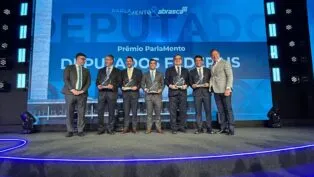 Esta é uma fotografia tirada em um evento formal de premiação, mostrando um grupo de homens, a maioria vestindo ternos escuros, em um palco.