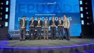 Esta é uma fotografia tirada em um evento formal de premiação, mostrando um grupo de homens, a maioria vestindo ternos escuros, em um palco.