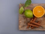Na foto há uma tábua de madeira com um limão, laranja e canela.