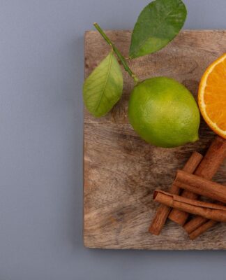 Na foto há uma tábua de madeira com um limão, laranja e canela.