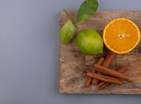 Na foto há uma tábua de madeira com um limão, laranja e canela.