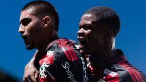 A foto em plano médio captura dois jogadores de futebol do time do Flamengo celebrando um momento de gol ou vitória com grande intensidade emocional.