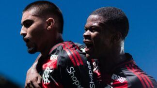 A foto em plano médio captura dois jogadores de futebol do time do Flamengo celebrando um momento de gol ou vitória com grande intensidade emocional.