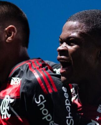 A foto em plano médio captura dois jogadores de futebol do time do Flamengo celebrando um momento de gol ou vitória com grande intensidade emocional.