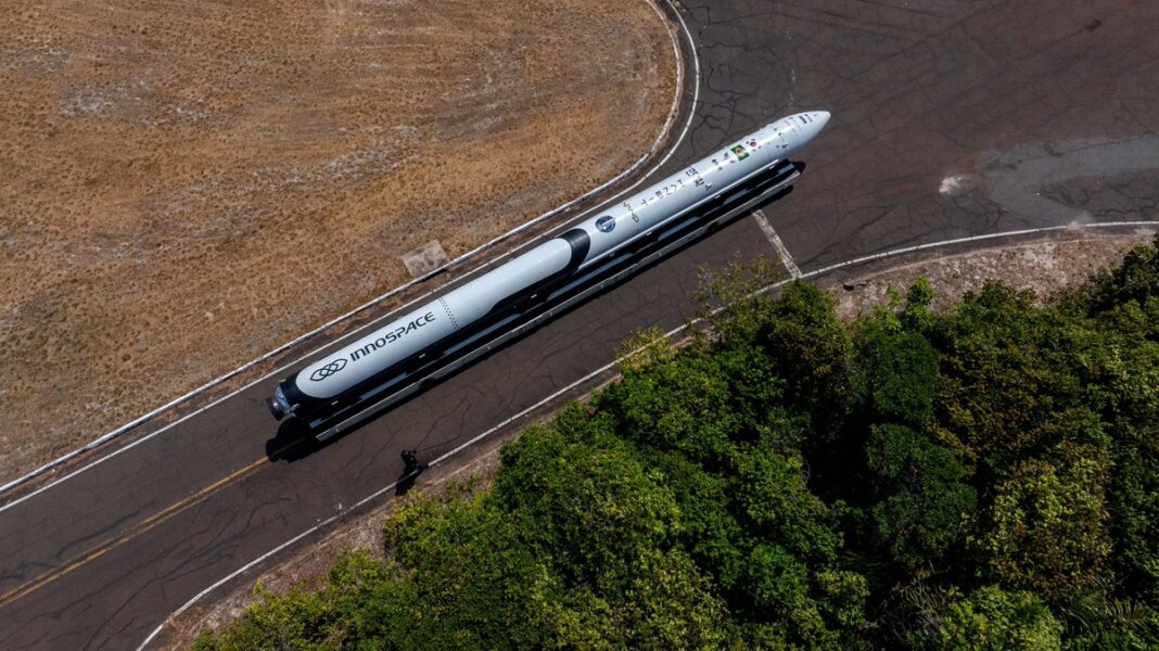 Esta é uma foto aérea (tirada de cima) que mostra um foguete sendo transportado por uma estrada ou pista em uma área predominantemente rural ou de vegetação.