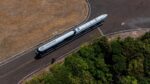 Esta é uma foto aérea (tirada de cima) que mostra um foguete sendo transportado por uma estrada ou pista em uma área predominantemente rural ou de vegetação.