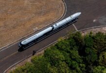Esta é uma foto aérea (tirada de cima) que mostra um foguete sendo transportado por uma estrada ou pista em uma área predominantemente rural ou de vegetação.