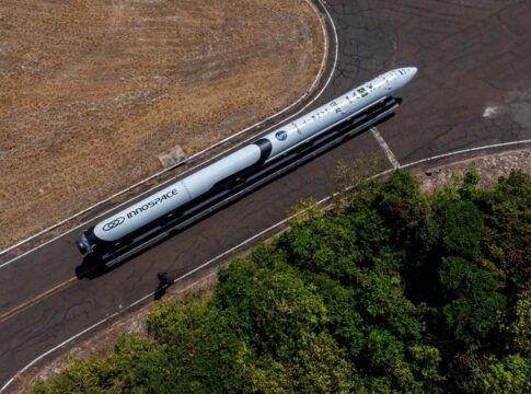 Esta é uma foto aérea (tirada de cima) que mostra um foguete sendo transportado por uma estrada ou pista em uma área predominantemente rural ou de vegetação.