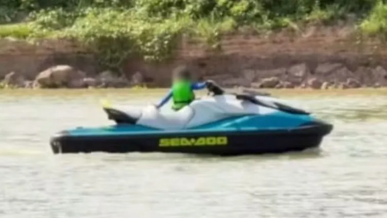 A imagem mostra uma criança muito pequena pilotando um jet ski em um corpo d'água, com o rosto borrado digitalmente para proteger sua identidade, conforme indicado pela nota do Conselho Tutelar sobre o episódio.